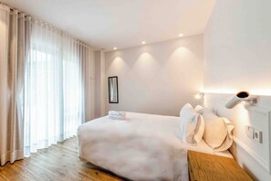 Quarto de hotel com cama, cortinas, mesa de cabeceira e luminária na parede.