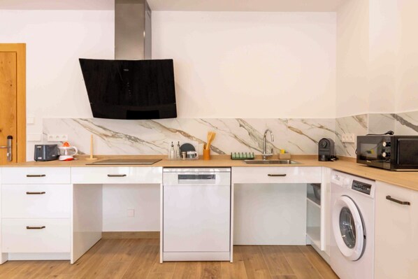 Uma cozinha compacta com lava-louças, micro-ondas e máquina de lavar, uma porta de madeira e painel de fundo em mármore.