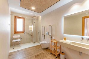 Uma casa de banho moderna com chuveiro envidraçado, sanita branca, prateleira de madeira e espelho grande.