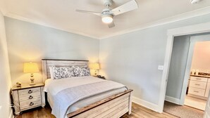 Ein Schlafzimmer mit einem hölzernen Bett, zwei Nachttischen mit Lampen, einem Deckenventilator und einer Tür zu einem Badezimmer.