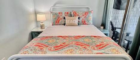 Un lit bien fait, recouvert d’une couvre-lit à motifs, avec une lampe de chevet et une décoration murale représentant des poissons.