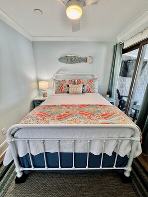 A neatly made bed with a patterned bedspread, a bedside lamp, and a decorative fish wall hanging. - Family Fun Getaway 4BR 2BA Short Walk To The Pier Outdoor Entertainment Space (Oak Island)