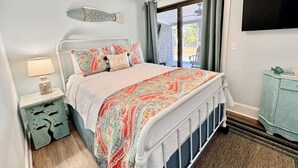 Ein Schlafzimmer mit Bett, Nachttisch, Lampe, einem Teppich mit Fischmotiv und Blick ins Freie.