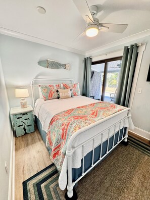 A bedroom with a bed, a nightstand, a ceiling fan, and a window with curtains. - Family Fun Getaway 4BR 2BA Short Walk To The Pier Outdoor Entertainment Space (Oak Island)