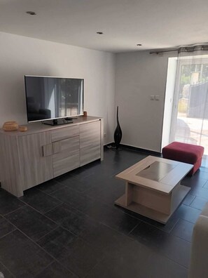 A modern living room with a flat-screen TV on a wooden cabinet, a minimalist coffee table, and a red ottoman. - Provençal and Mediterranean-style house, 167 square meters (Marseille)