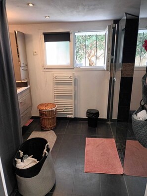 Een badkamer met een raam, een radiator, een rieten mand, een zwarte prullenbak en een grijze opbergmand.