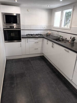 A modern kitchen with a microwave, oven, gas stove, and a window. - Provençal and Mediterranean house 167 sqm (Marseille)
