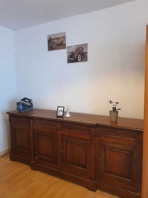 Une pièce comprenant un meuble en bois, un tableau représentant une voiture, une petite maquette d’une tour et une plante en pot.