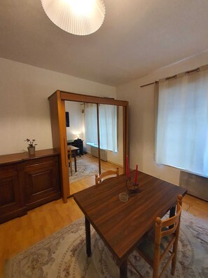 Un comedor con mesa de madera, sillas, un espejo, una planta en maceta y una ventana con cortinas.