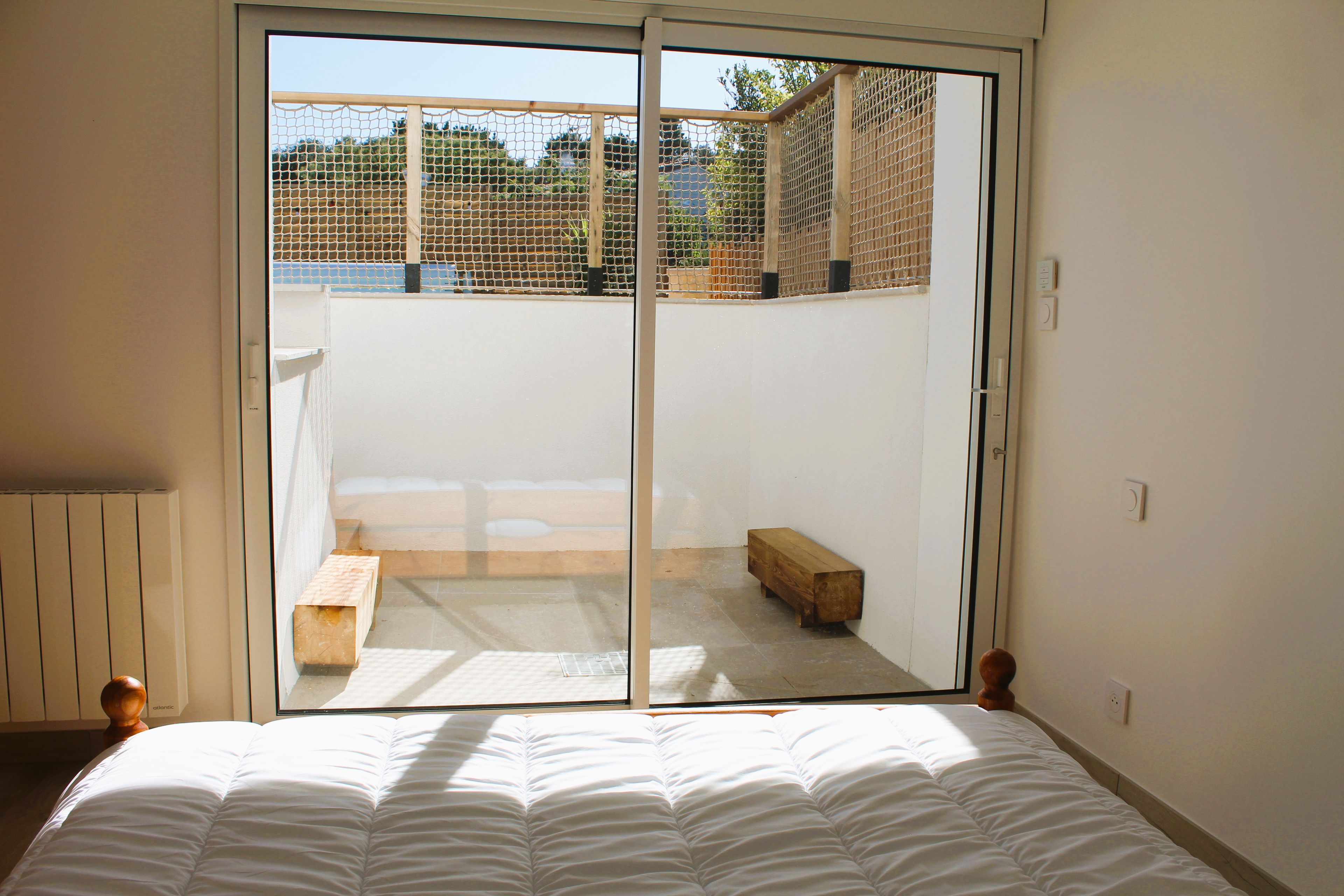 A bedroom with a bed, a sliding glass door leading to a balcony with a wooden bench and a fence.