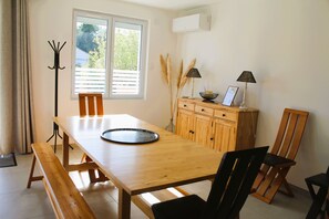 A dining area with a wooden table, chairs, a bench, a cabinet with decorative items, and a window with blinds. - Charm & Relaxation: Family Home with Heated Pool (Jard-sur-Mer)