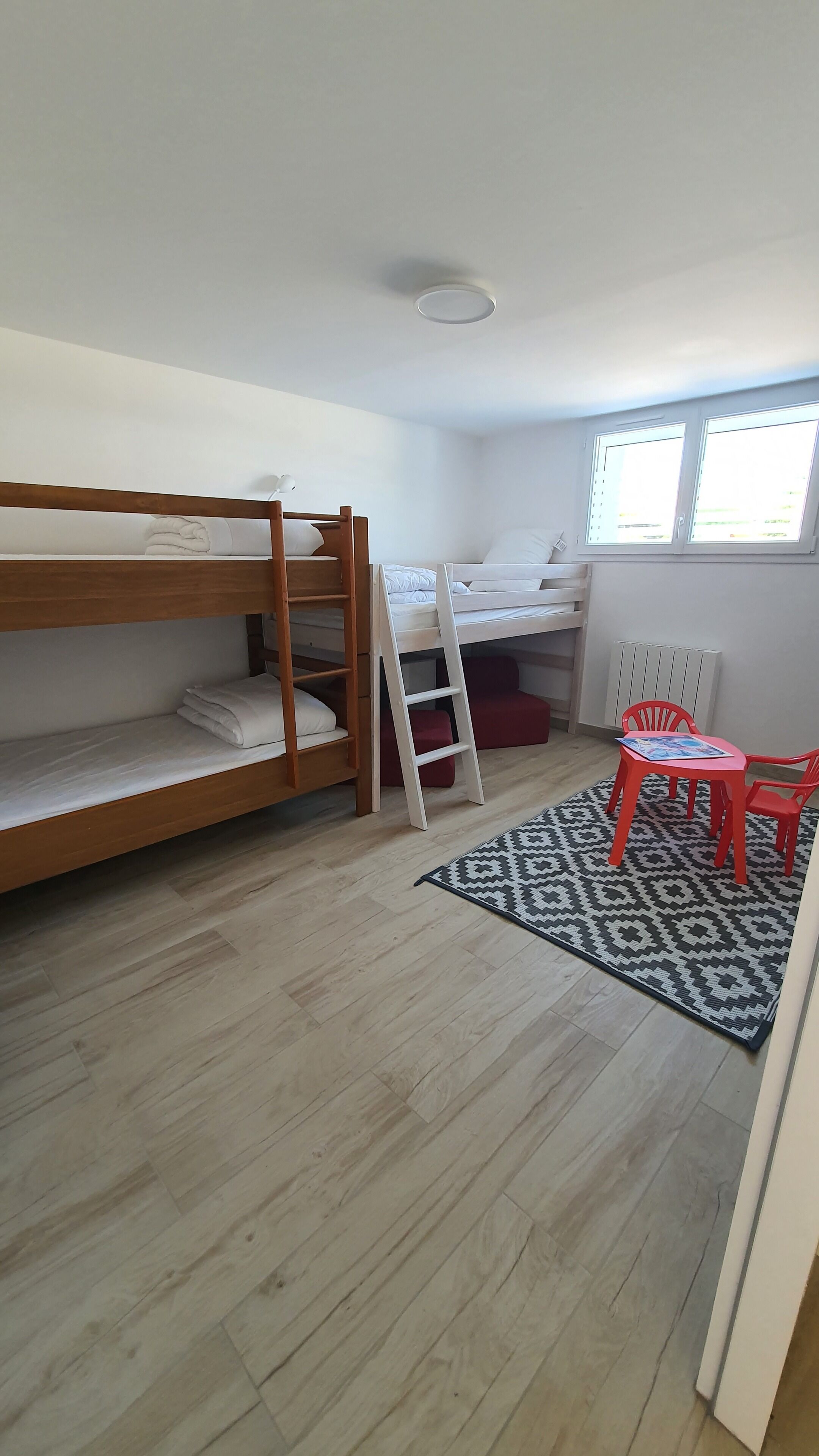 Una habitación con dos literas, una silla roja, una mesita y una alfombra estampada.