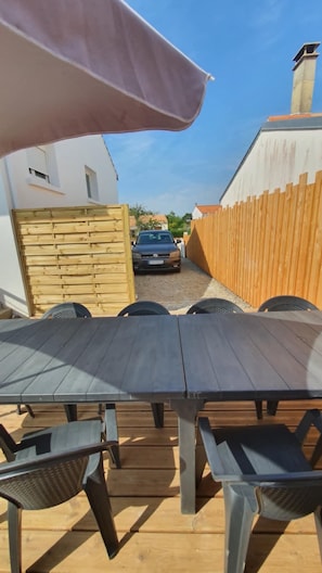 A wooden deck with a table and chairs, a car parked in the background, and a wooden fence.