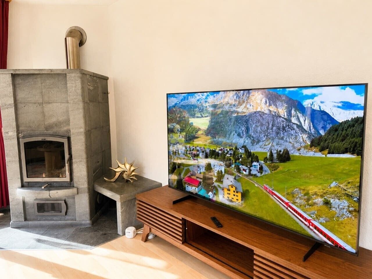 Ett vardagsrum med en öppen spis i sten, en platt-TV placerad på ett träställ och en fjärrkontroll på stället.