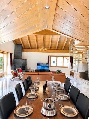 A spacious dining area with a high wooden ceiling, a fireplace, and a television.