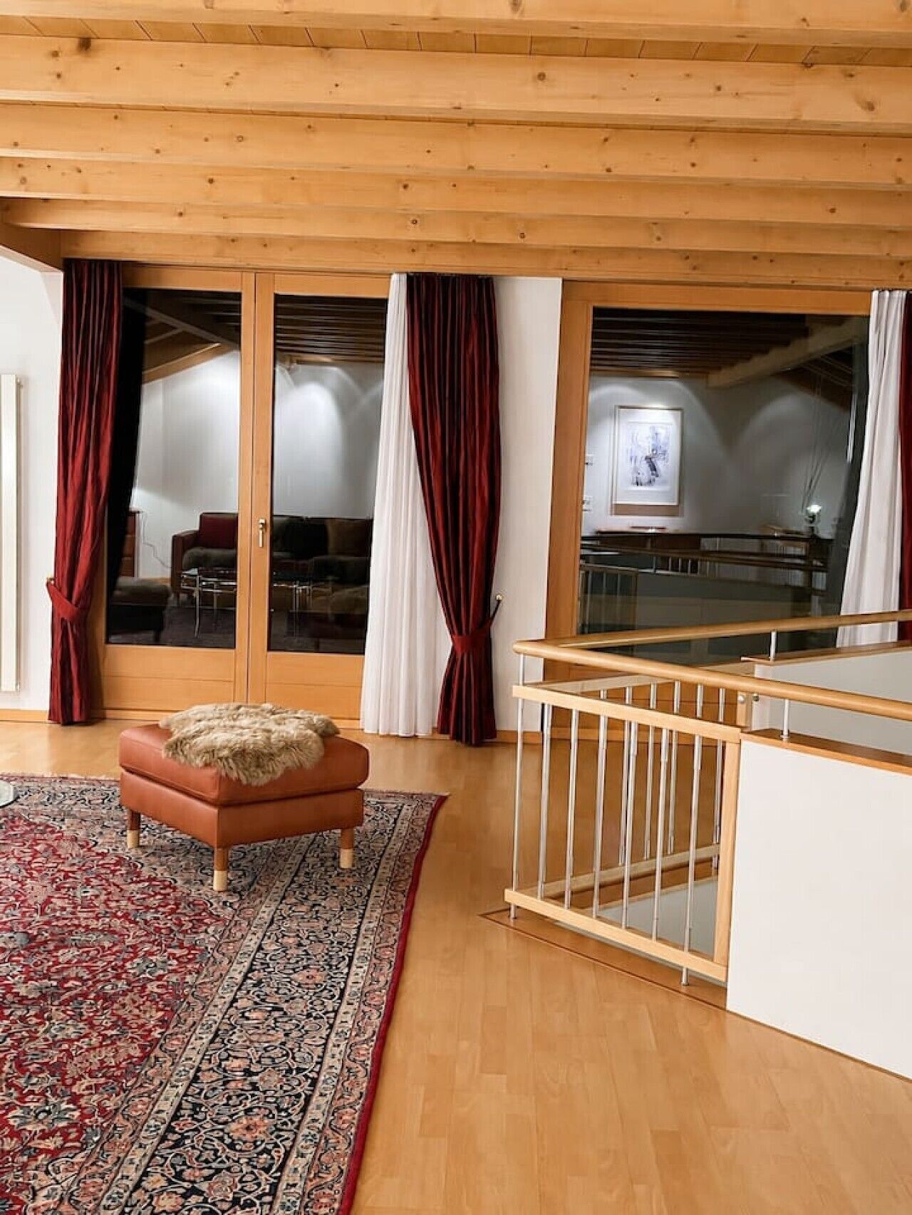 A room with a wooden ceiling, a red and white patterned rug, a brown leather sofa, and a wooden railing.