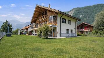 A two-story building with a balcony, a grassy yard, and a mountain backdrop.