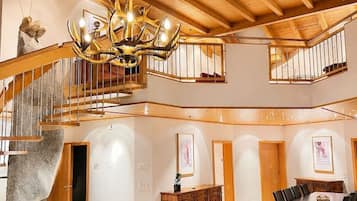 A spacious interior with a high ceiling, a grand chandelier, a staircase, a dining area, and a seating area.