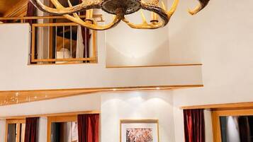 A chandelier with antler motifs, a framed picture of a forest scene, and a wooden cabinet.