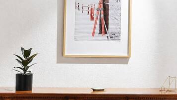 Ein gerahmtes Bild einer verschneiten Landschaft mit Ski an der Wand, eine Topfpflanze und eine Holzkommode mit Stühlen.