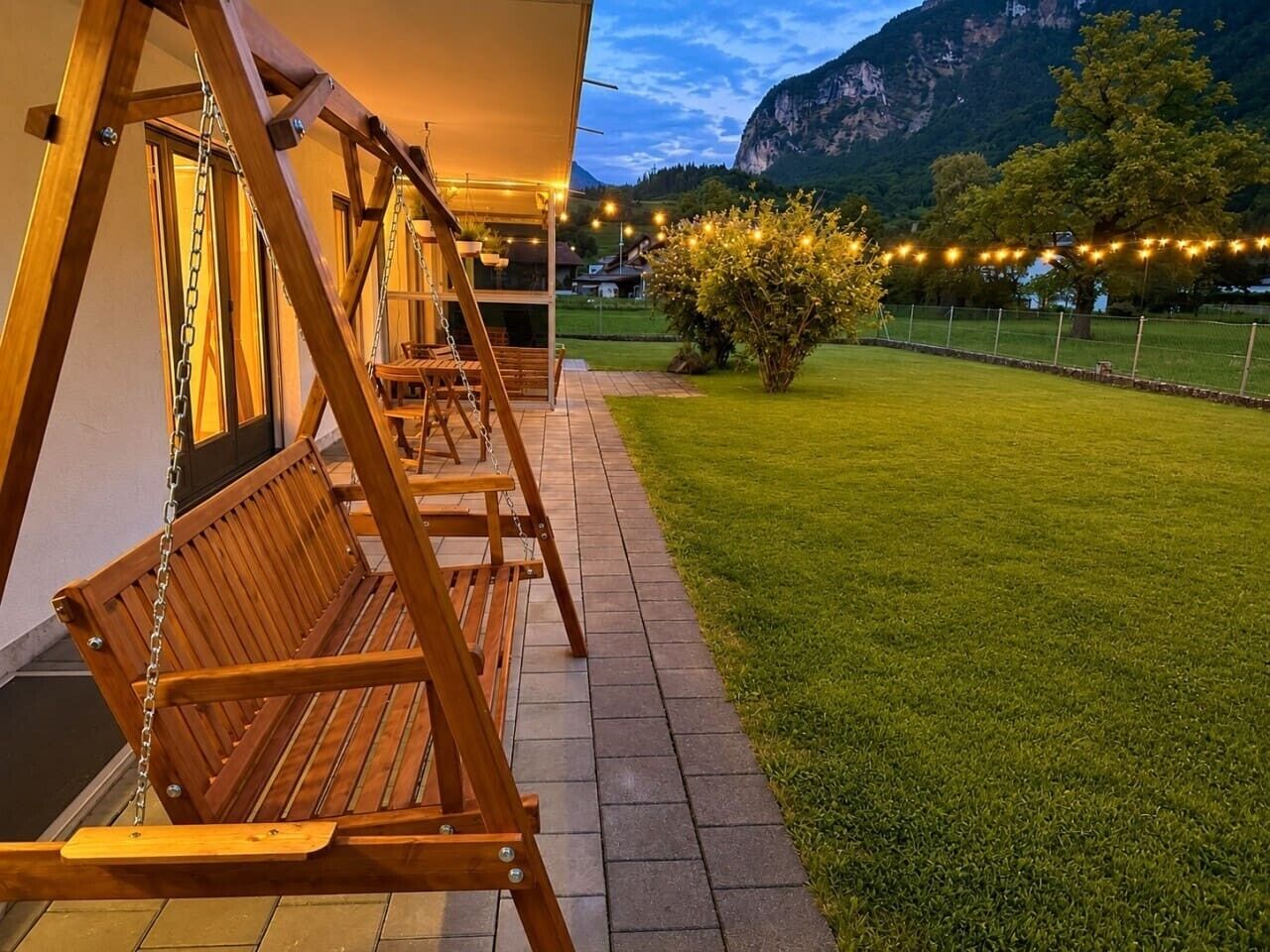 A wooden swing set in a well-maintained garden with a mountain backdrop.