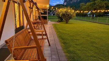 A wooden swing set in a well-maintained garden with a mountain backdrop.