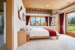 A bedroom with a bed, wooden headboard, a bedside table, a lamp, and a view of the outdoors. - 7BR Luxury Chalet near Interlaken • AC • 18 guests (Meiringen)