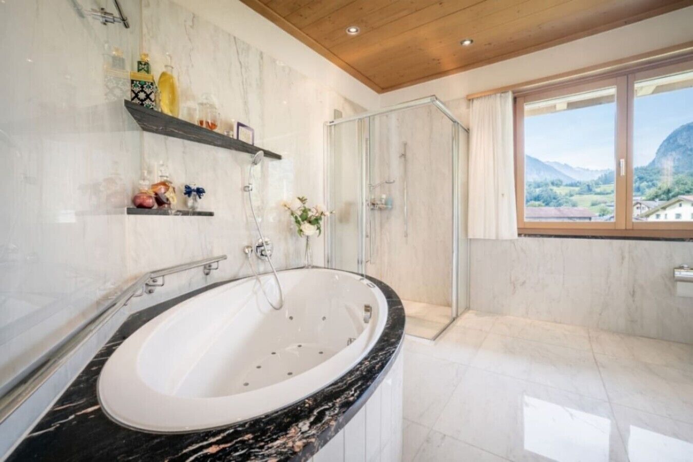 A bathroom with a large bathtub, a glass shower enclosure, and a view of the outdoors through a window.