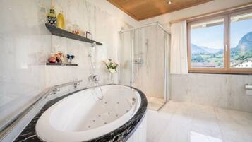 A bathroom with a large bathtub, a glass shower enclosure, and a view of the outdoors through a window.