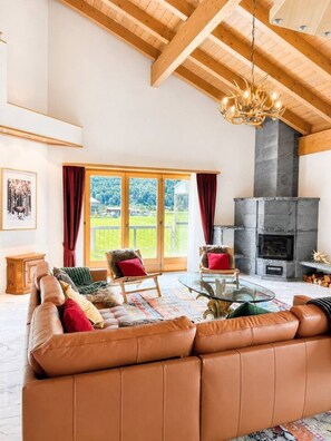 A spacious living room with a leather sofa, a fireplace, and a large window with curtains.