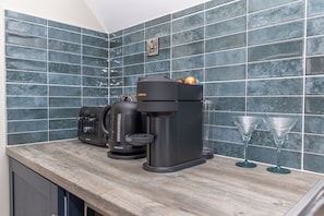 Una cocina con una cafetera, un hervidor y dos vasos sobre la encimera.