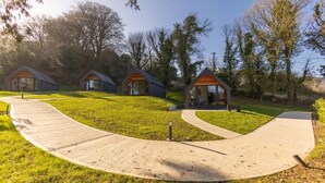 A row of modern cabins with a paved walkway leading to them, surrounded by trees. - Narrow Water Lodges (Dundalk)