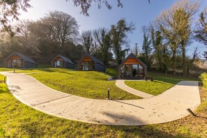 A row of modern cabins with a paved walkway leading to them, surrounded by trees.