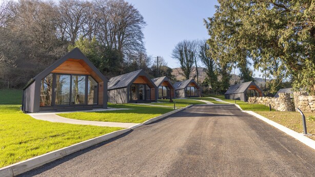 A row of modern cabins with large windows, a paved driveway, and a stone wall. - Narrow Water Lodges (Dundalk)