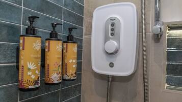 Un baño con cabezal de ducha Triton blanco, tres botellas de gel de baño y un dispensador de jabón de manos en la pared.