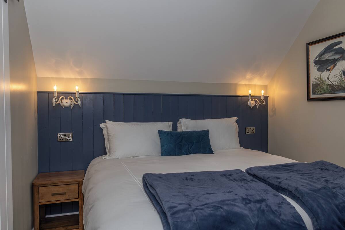 A bedroom with a bed, bedside tables, wall-mounted lights, and a framed picture.