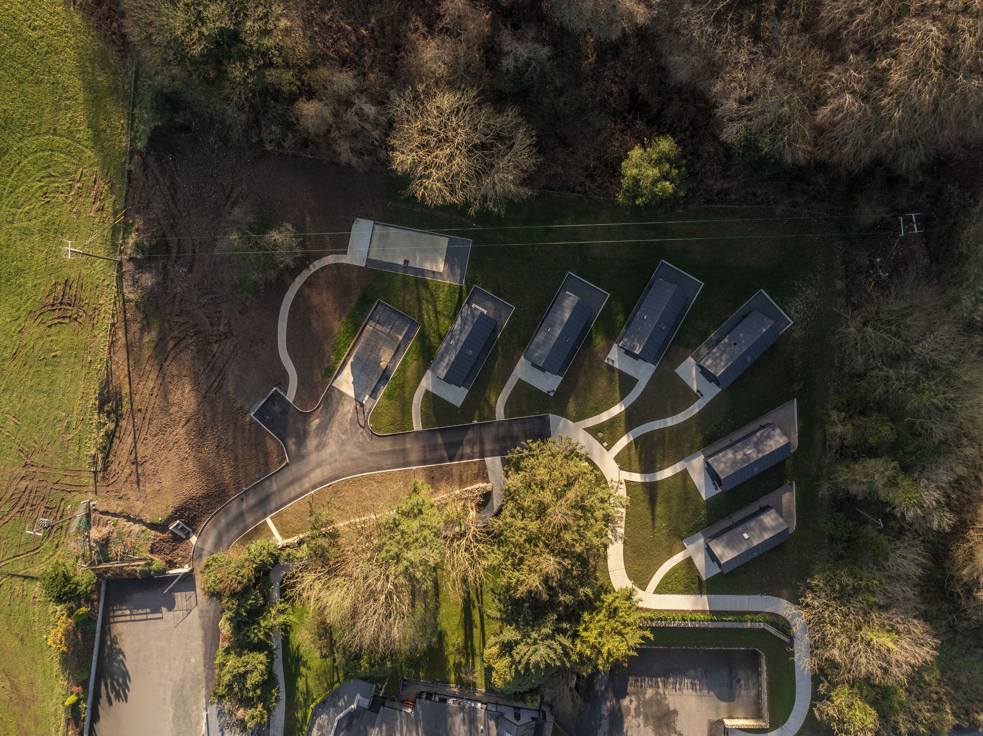 Vista aérea de uma área residencial com uma rua central, cercada por casas com garagens anexas, e uma pequena área de parque com árvores.