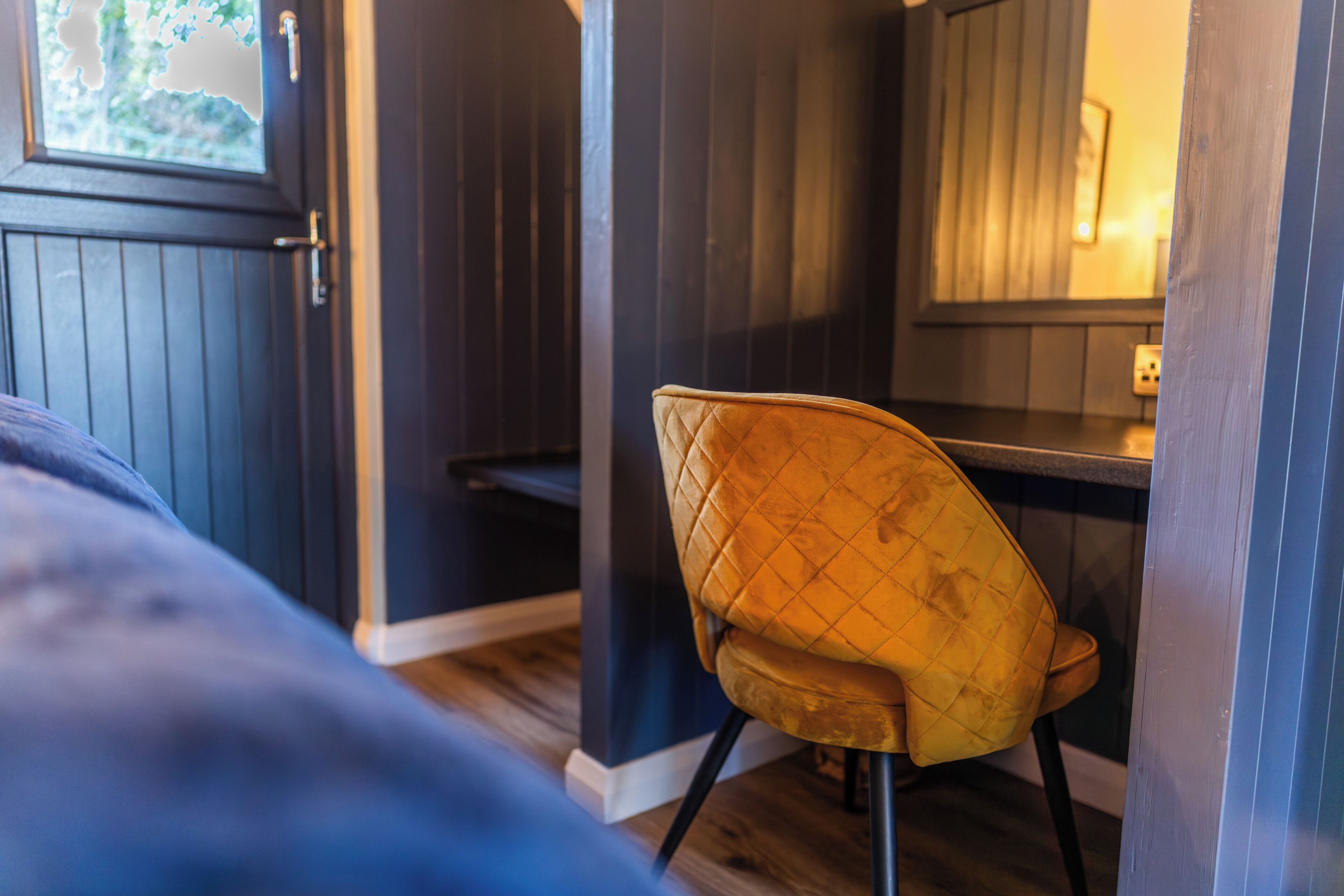 Ein Zimmer mit einem Bett, einem gelben Sessel, einem Holztisch und einer Tür mit Fenster.