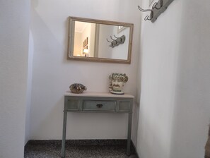 Een hoekje met een spiegel, een klein tafeltje met decoratieve items, en een haak aan de muur.