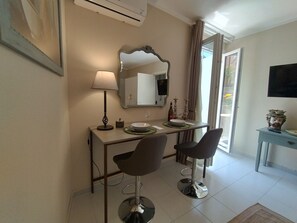 Una habitación con una mesa de comedor, dos sillas, un espejo, una lámpara, un televisor y un florero sobre una mesita auxiliar.
