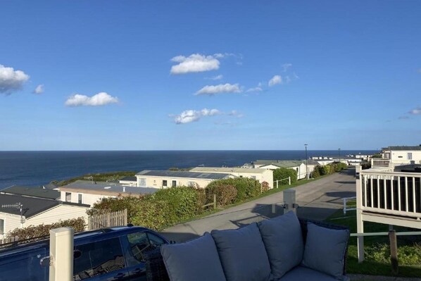 A seaside view with a row of white mobile homes, a parked car, and a blue car in the foreground.