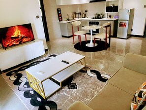 Ein modernes Wohnzimmer mit Kamin, einem Essbereich mit Tisch und Stühlen sowie einer Küche mit Geräten.