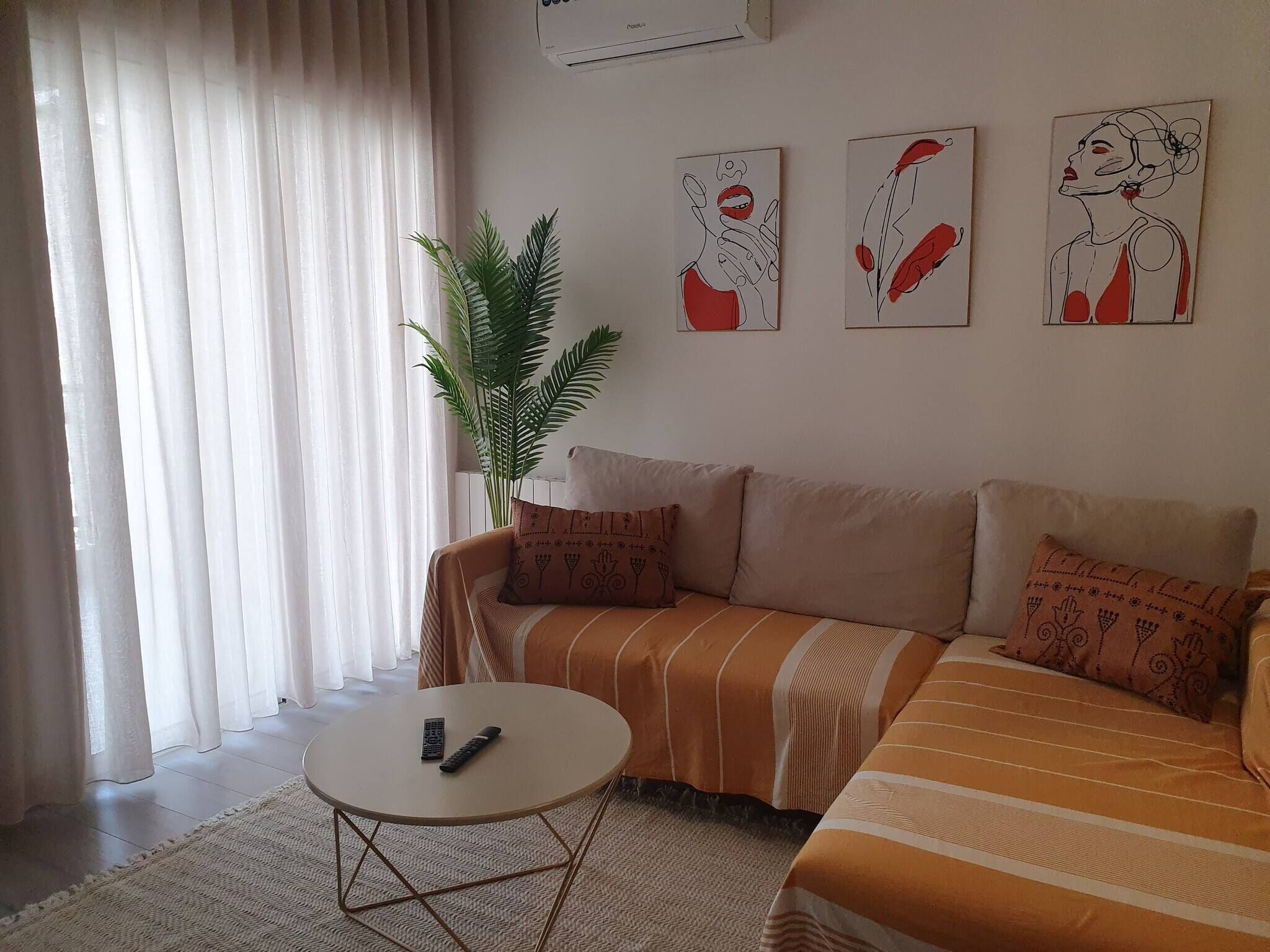 A living room with a sofa, a small round table, a potted plant, and three artworks on the wall.