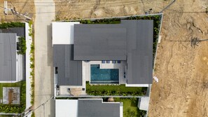 Eine Vogelperspektive auf ein modernes Haus mit Swimmingpool, einer überdachten Terrasse und einem gepflegten Garten.
