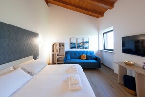 A modern hotel room with a bed, a blue sofa, a TV, and a window. - Farmhouse nestled in the countryside on the outskirts of Rome. (Lazio)
