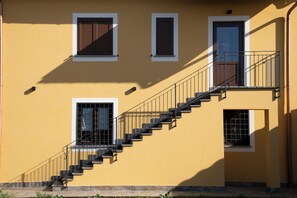 A building with a yellow exterior, a staircase with metal railings, and three windows with shutters.