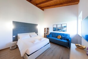 A modern hotel room with a bed, a blue sofa, a wooden ceiling, and a large window. - Farmhouse nestled in the countryside on the outskirts of Rome. (Lazio)