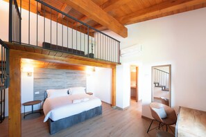 A bedroom with a bed, a chair, a wooden ceiling, and a staircase.