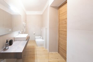 Et moderne badeværelse med et stort spejl, en vask, et toilet og et bruseområde.