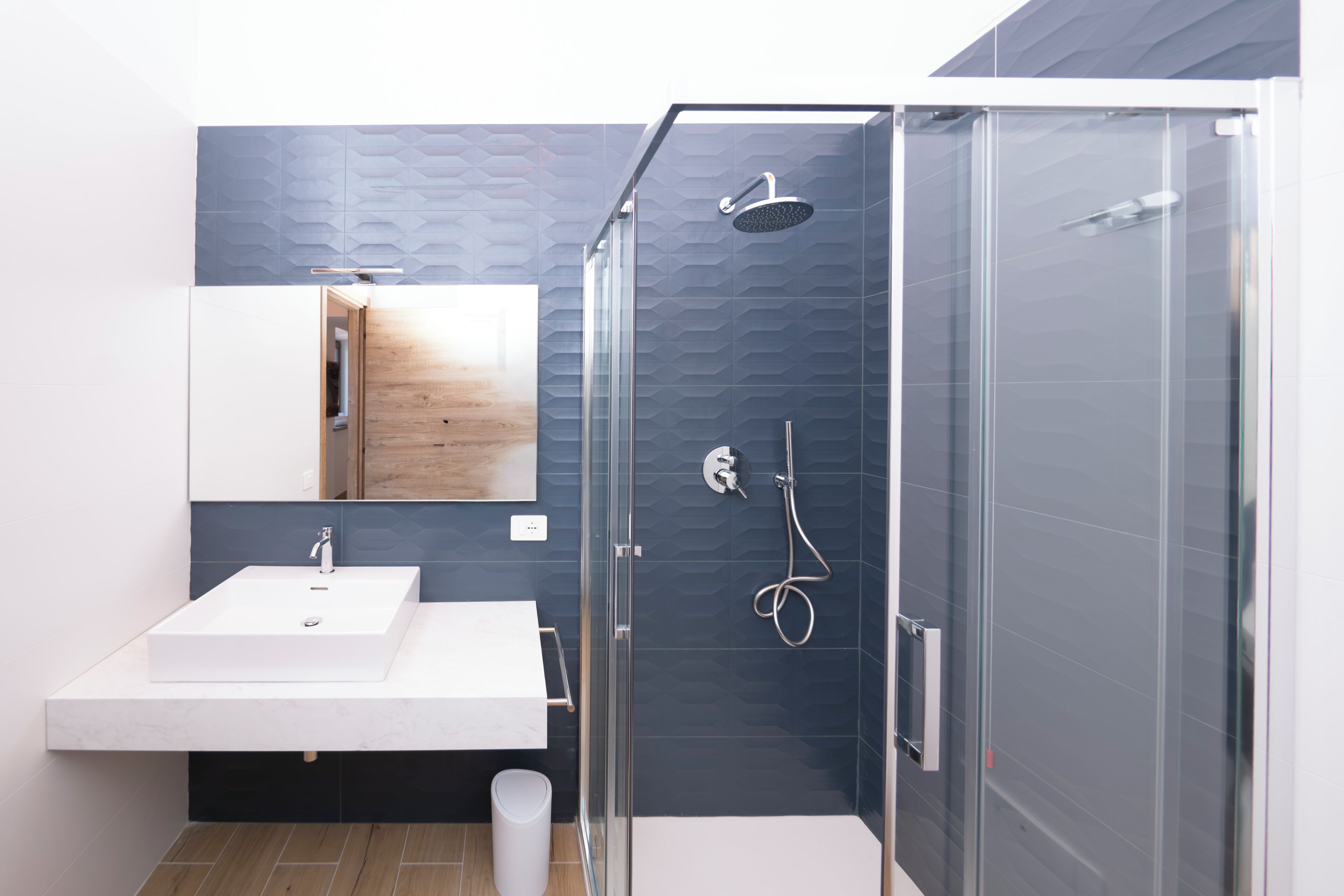 A modern bathroom with a glass-enclosed shower, a white sink, and a wooden vanity.